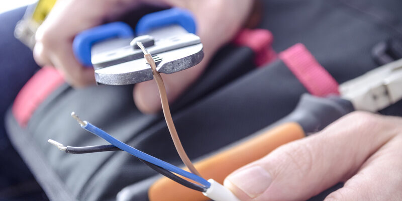 Closeup of worker's hands cutting electric wires with pliers.